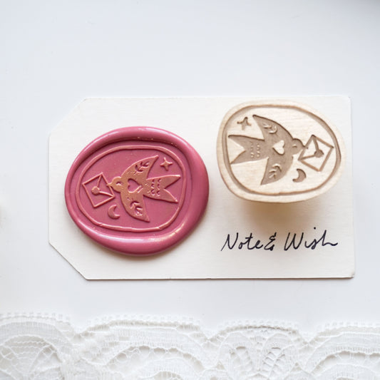 A wax seal stamp set featuring a pink wax seal impression with a bird and envelope design