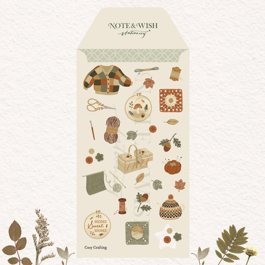 A tall cream-colored sticker sheet decorated with autumn-themed illustrations including a plaid cardigan, scissors, yarn, leaves, acorns and a teapot. 