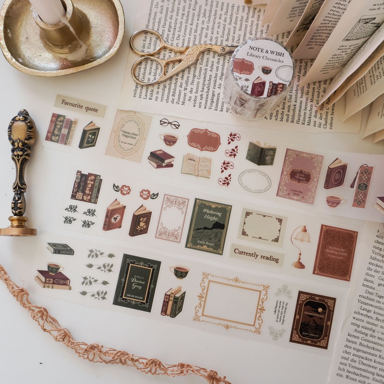 Sheet of decorative PET tape dark academia style stickers with book-themed designs on a surface with a candle and scissors. Books include Little Women, Pride and Prejudice, Wuthering Heights and Frankenstein.