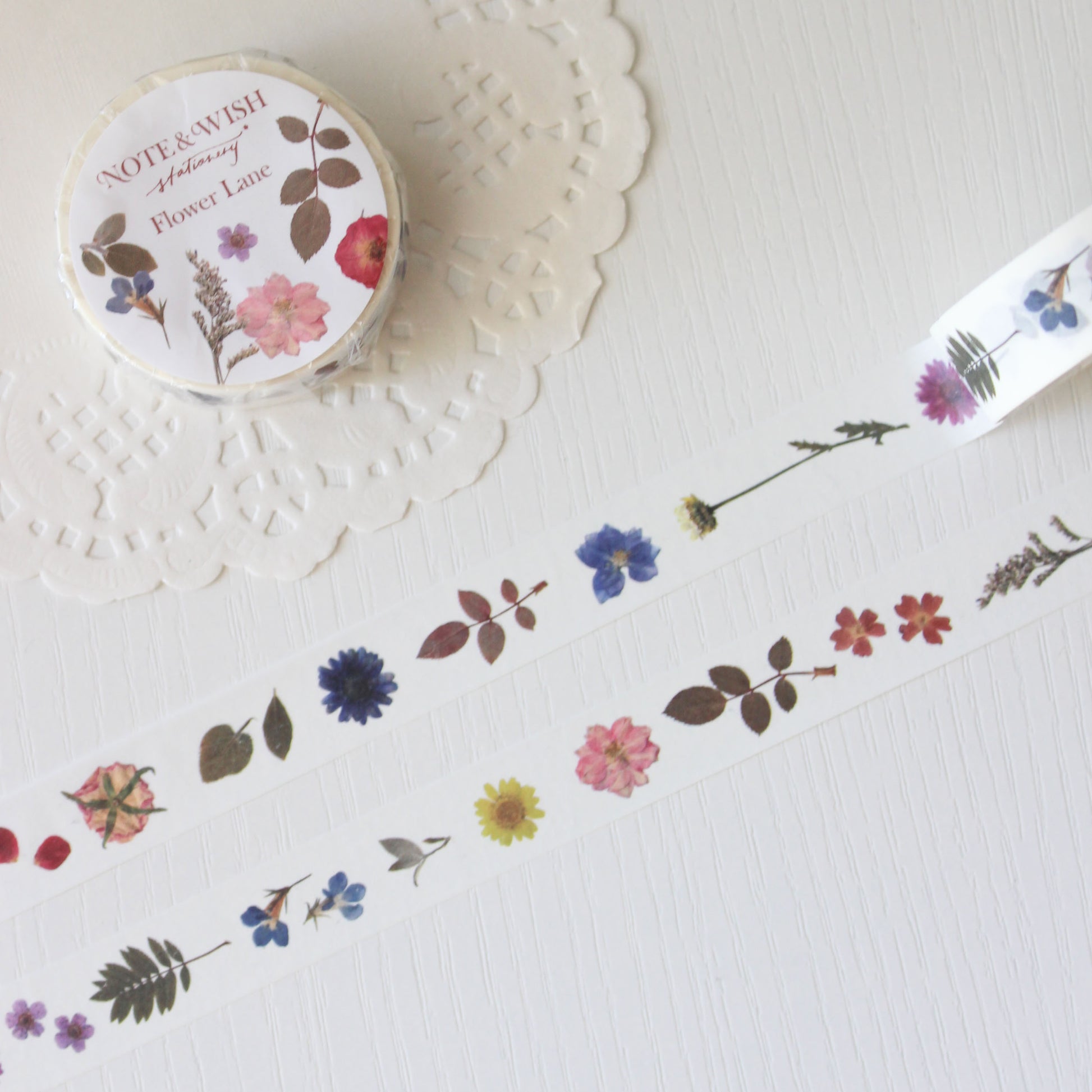Roll of floral washi tape on a white surface with a decorative doily.