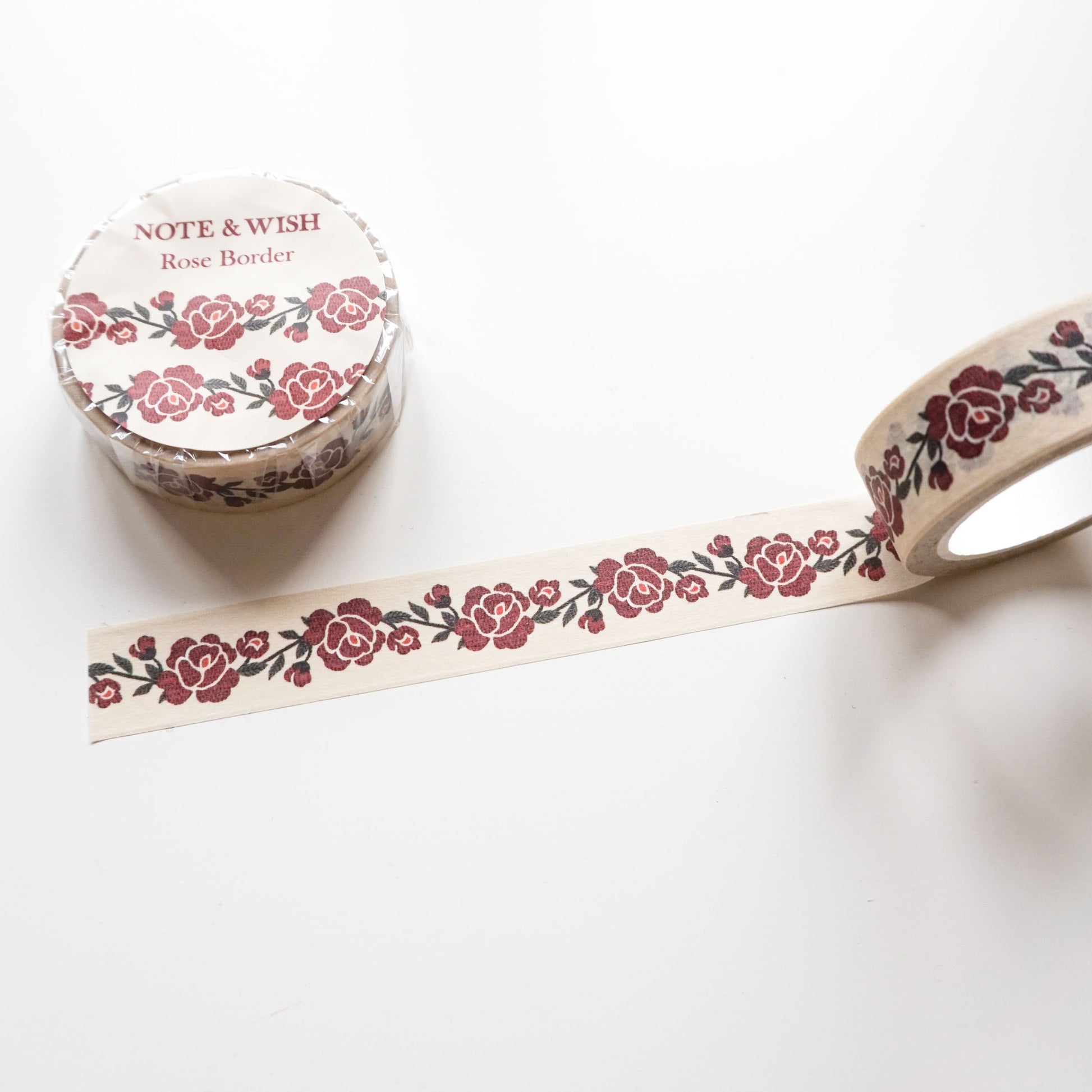 A roll of decorative washi tape with a repeating red rose and green vine border pattern